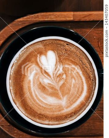 Coffee with heart latte art in a dark ceramic cup on a wooden tray. White foam forms a heart on coffee in a dark cup, with the coffee presented on wooden tray Coffee with heart latte art in a dark ceramic cup on a wooden tray. White foam forms a heart on coffee in a dark cup, with the coffee presented on wooden tray 143407059