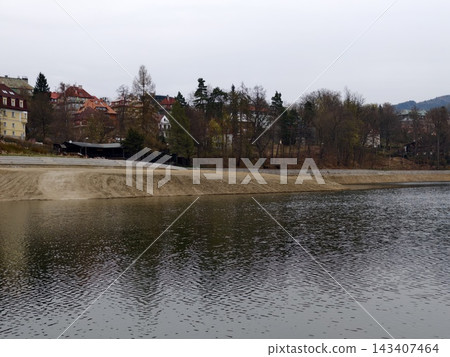 Serene lakeside with forests. Tranquil coast featuring distant homes and gentle flowing water Serene lakeside with forests. Tranquil coast featuring distant homes and gentle flowing water 143407464