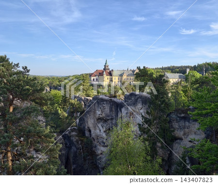 Imposing fortress amid rugged terrain. Historic castle set against towering rocks and shadowy valleys Imposing fortress amid rugged terrain. Historic castle set against towering rocks and shadowy valleys 143407823