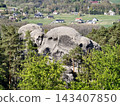 Eroded rock formations. Eroded sandstone blocks with lush moss and distant cottages amid rolling pastures 143407850