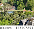 Charming rural dwelling nestled beside calm pond framed by verdant hedge and vibrant spring growth 143407854