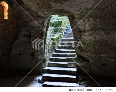 Cave interior stone staircase carved from rock walls moss covered light filtering through opening illuminates rough texture and ancient passageway for adventurous exploration 143407869