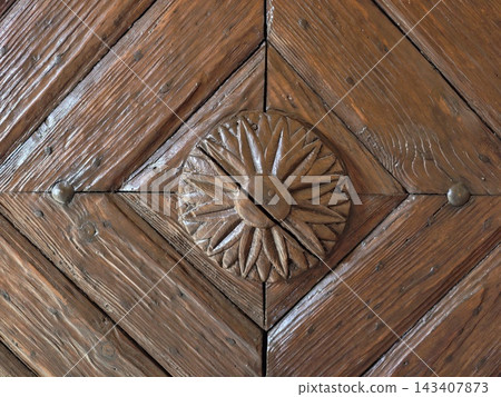 Rectangular wooden door panel featuring carved geometric triangles and riveted studs in weathered brown wood with diamond centerpiece, intricate bevels, aged texture, rustic architectural detail Rectangular wooden door panel featuring carved geometric triangles and riveted studs in weathered brown wood with diamond centerpiece, intricate bevels, aged texture, rustic architectural detail 143407873