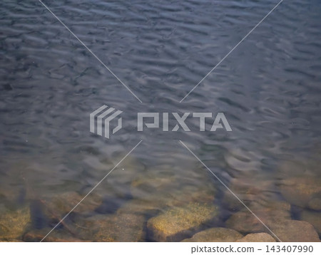 Night ocean water over rocky shoreline with visible submerged stones, faint blue glow, and gentle surf under moonlight Night ocean water over rocky shoreline with visible submerged stones, faint blue glow, and gentle surf under moonlight 143407990