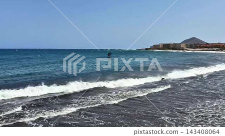 A stunning coastal scene features a kite surfer gliding over the clear blue waters of the ocean A stunning coastal scene features a kite surfer gliding over the clear blue waters of the ocean 143408064