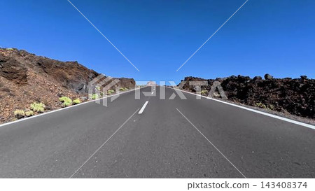 A picturesque scenic road winding through a volcanic lava landscape beneath a clear blue sky A picturesque scenic road winding through a volcanic lava landscape beneath a clear blue sky 143408374