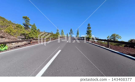 A beautiful scenic mountain road surrounded by lush green pine trees under a clear blue sky A beautiful scenic mountain road surrounded by lush green pine trees under a clear blue sky 143408377