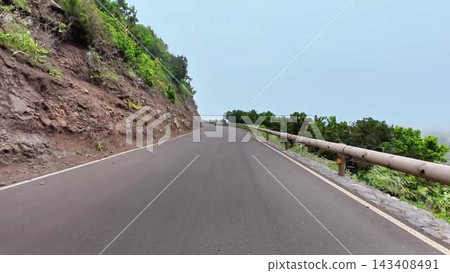 A beautiful and scenic winding road that travels through lush greenery and rocky terrain A beautiful and scenic winding road that travels through lush greenery and rocky terrain 143408491