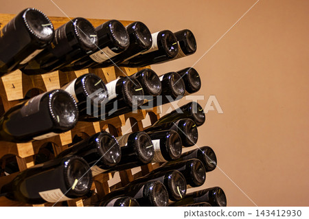 Storing wine bottles horizontally on a wooden rack, indicating careful cellar management and the aging process of red or white varietals within a winery or personal collection Storing wine bottles horizontally on a wooden rack, indicating careful cellar management and the aging process of red or white varietals within a winery or personal collection 143412930