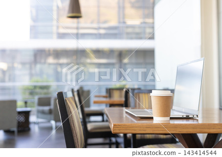 Paper coffee cup sitting on wooden table beside slim laptop at modern cafe, copy space Paper coffee cup sitting on wooden table beside slim laptop at modern cafe, copy space 143414544