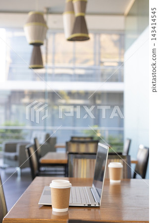 Open silver laptop sitting on wooden table with paper coffee cup near glass wall Open silver laptop sitting on wooden table with paper coffee cup near glass wall 143414545