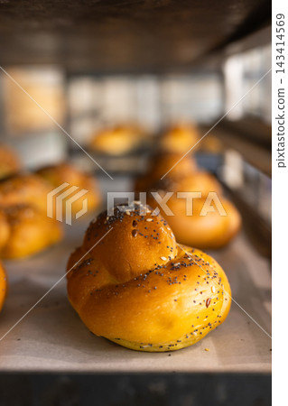 Golden knot roll resting on parchment-lined metal tray on bakery rack, gleaming with poppy seeds Golden knot roll resting on parchment-lined metal tray on bakery rack, gleaming with poppy seeds 143414569