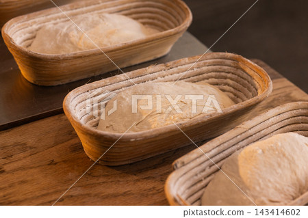 Oval woven bannetons holding three flour-dusted loaves of proofing dough on wooden countertop 143414602