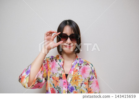 一位身穿花襯衫、戴著太陽眼鏡的女士,以白色背景為襯托,拍攝了一張肖像照。 一位身穿花襯衫、戴著太陽眼鏡的女士,以白色背景為襯托,拍攝了一張肖像照。 143415659