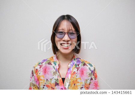 一位微笑的女士身穿花襯衫,戴著太陽眼鏡,背景為白色。 一位微笑的女士身穿花襯衫,戴著太陽眼鏡,背景為白色。 143415661