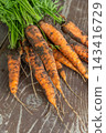 Freshly harvested carrots with dirt on wooden table showcasing vibrant orange colors and leafy tops perfect for healthy meals and snacks 143416729