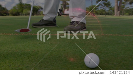Lining up golfer in light-trousers dark-golf-shoes on green, with golf ball, putter, red-rim cup Lining up golfer in light-trousers dark-golf-shoes on green, with golf ball, putter, red-rim cup 143421134