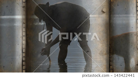 Bending silhouetted man in cap and shorts handling small fish in shallow water with film borders Bending silhouetted man in cap and shorts handling small fish in shallow water with film borders 143422441