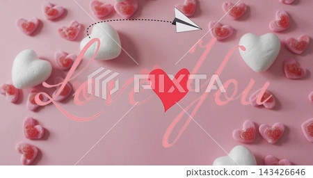Showing Valentine display on pink table marshmallows pink gummy hearts cursive Love You paper plane 143426646