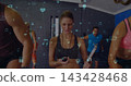 Leading female coach in tank top timing cardio in studio, holding stopwatch, clipboard, AR overlay 143428468