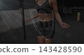 Jumping mid-adult woman in dark sportswear, gripping jump-rope in dim gym with rig, shield overlay 143428590