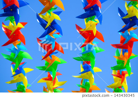 A vibrant, colorful array of pinwheels suspended against a clear blue sky in a symmetrical composition A vibrant, colorful array of pinwheels suspended against a clear blue sky in a symmetrical composition 143430345