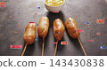 Displaying four battered corn dogs on skewers glowing on dark board, with mustard bowl, play badges 143430838