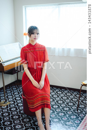 房間裡坐著一位穿著紅色洋裝的女子。 143431878