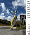 A yellow dinosaur sculpture towering against a blue sky, and the surrounding outdoor scenery. 143432016