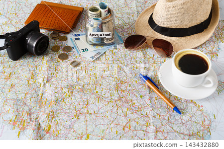 Items are laid out on a map for travel planning. A camera, money, coins, a notebook, sunglasses, a hat, and coffee are present. Elements suggest preparation for an adventure or trip. Items are laid out on a map for travel planning. A camera, money, coins, a notebook, sunglasses, a hat, and coffee are present. Elements suggest preparation for an adventure or trip. 143432880