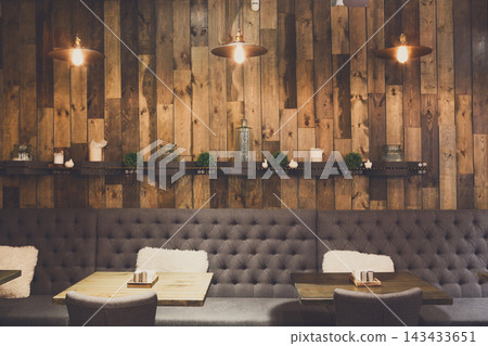 A warm dining area with wooden walls and comfortable seating. Tables are arranged for guests to enjoy meals together. Soft lights create an inviting atmosphere. A warm dining area with wooden walls and comfortable seating. Tables are arranged for guests to enjoy meals together. Soft lights create an inviting atmosphere. 143433651