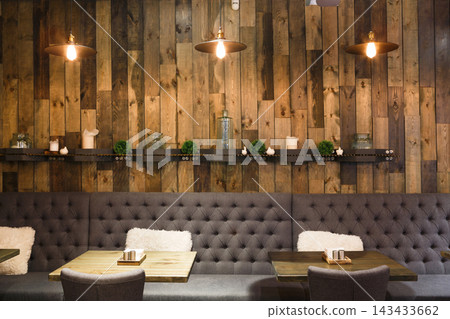 The interior showcases a cozy and inviting atmosphere with tufted gray seating, wooden wall panels, and warm lighting, ideal for casual meetings or socializing in a cafe setting. The interior showcases a cozy and inviting atmosphere with tufted gray seating, wooden wall panels, and warm lighting, ideal for casual meetings or socializing in a cafe setting. 143433662