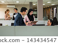 Diversity group of colleagues in open space office. Woman in hijab sharing information on digital tablet with Asian businessman while others working and interacting in background 143434547