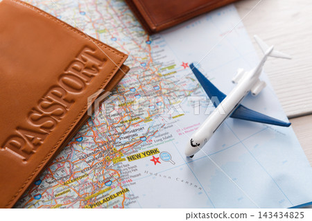 A passport and an airplane model sit on a map showing New York. The items are arranged on a table, illustrating travel plans. The map highlights the city for the journey. 143434825