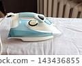 Close-up view of a steam iron resting on a blue shirt, illustrating garment care, wrinkle removal, ironing and everyday household maintenance. 143436855