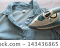 Steam iron pressing a blue shirt on a bed, focusing on garment care, wrinkle removal and everyday household ironing. 143436865