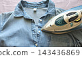 Blue shirt and steam iron placed on a bed at home, illustrating everyday clothing care, ironing and household laundry routine. 143436869