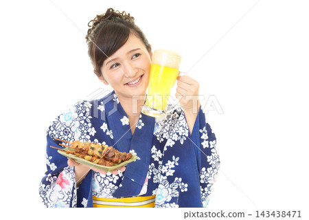 一位身穿浴衣的女子手拿啤酒和烤雞串。 一位身穿浴衣的女子手拿啤酒和烤雞串。 143438471