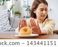 glazed donuts on plate with Asian woman making stop hand gesture in background, refusing unhealthy sugary food for diet and weight loss healthy concept. 143441151
