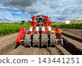 rear view of a modern agricultural seeder and tilling machine working in a freshly plowed dirt field on an Asian rural farm under cloudy blue sky. 143441251