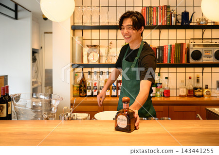 一位調酒師微笑地在吧台為顧客服務。 一位調酒師微笑地在吧台為顧客服務。 143441255