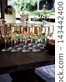 multiple champagne flutes with sparkling wine lined up on a dark wooden table 143442400