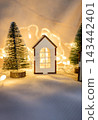 Miniature wooden toy house with Christmas trees and glowing lights. 143442401