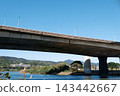Concrete elevated bridge spanning a river under clear blue sky with green hills 143442667