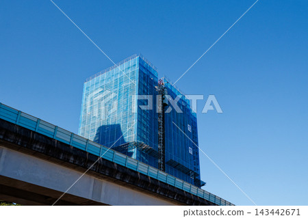 Blue netting covers a high-rise under construction beside an elevated viaduct Blue netting covers a high-rise under construction beside an elevated viaduct 143442671