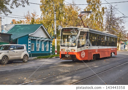 ULYANOVSK. russia. September 30, 2026. The tram travels along a city street past a wooden house. ULYANOVSK. russia. September 30, 2026. The tram travels along a city street past a wooden house. 143443358