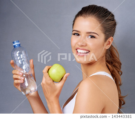 Water, apple and portrait of happy woman on gray background for training, exercise and workout. Fitness, studio and person with fruit for vitamins, diet and detox with health, wellness or lose weight Water, apple and portrait of happy woman on gray background for training, exercise and workout. Fitness, studio and person with fruit for vitamins, diet and detox with health, wellness or lose weight 143443381