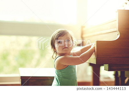Girl, child and playing on piano in house for musical development, learning and growth of motor skills or creativity. Toddler, instrument and playful in home for entertainment, education and sound. Girl, child and playing on piano in house for musical development, learning and growth of motor skills or creativity. Toddler, instrument and playful in home for entertainment, education and sound. 143444113