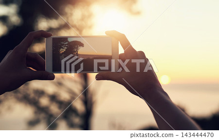 Person, hands and phone for picture in nature at sunset, vacation with memory of horizon. Mobile photographer, ui screen and summer scene with tree at dusk, beach holiday with creativity in Mauritius Person, hands and phone for picture in nature at sunset, vacation with memory of horizon. Mobile photographer, ui screen and summer scene with tree at dusk, beach holiday with creativity in Mauritius 143444470