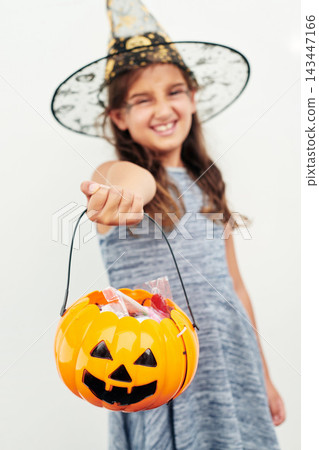 Halloween, pumpkin and child portrait with costume for fantasy, birthday party and candy in studio. Jack o lantern, sweets and young girl with creative fashion and witch clothes by white background Halloween, pumpkin and child portrait with costume for fantasy, birthday party and candy in studio. Jack o lantern, sweets and young girl with creative fashion and witch clothes by white background 143447166